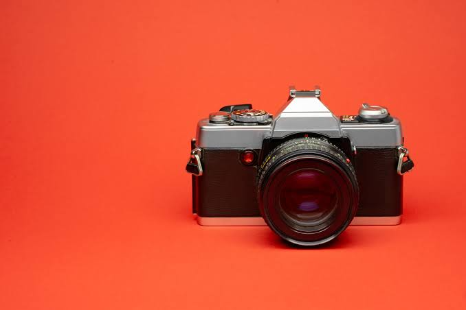 A camera and lens on a red background.